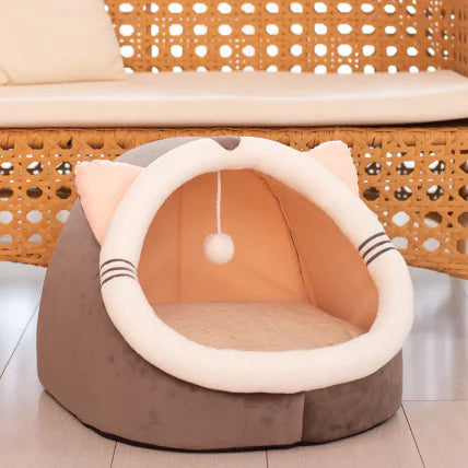 Cat-shaped pet bed with a ball on top, placed on a wooden floor.