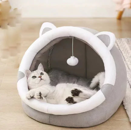 Cat lying in a gray and white pet bed with cat ears on a wooden floor.