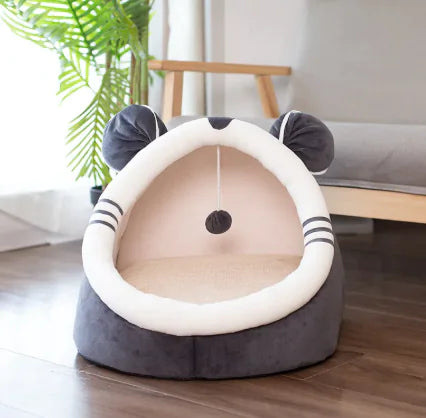 Cat-shaped pet bed on a wooden floor with a plant in the background